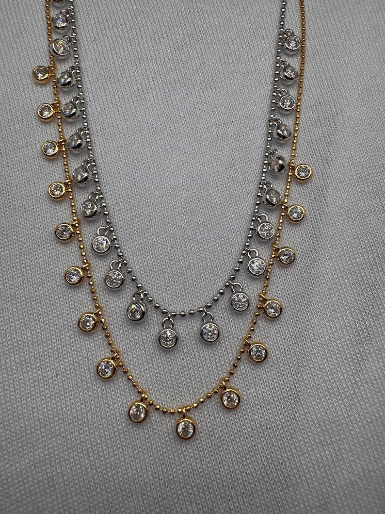 May include: A layered necklace with a gold chain and two silver chains. Each chain has small round clear stones hanging from it.