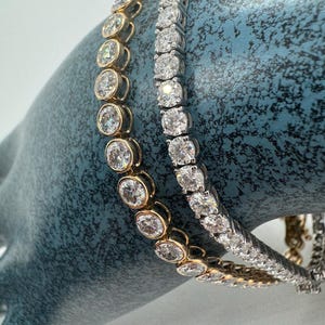 Two diamond tennis bracelets, one in yellow gold and one in white gold. Both bracelets feature round brilliant cut diamonds set in a pave setting.