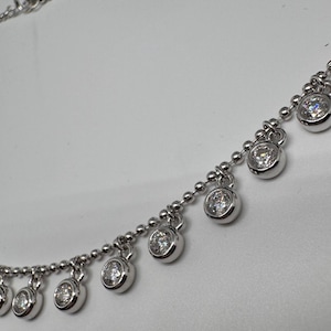 May include: A silver chain necklace with small round clear stones dangling from it.