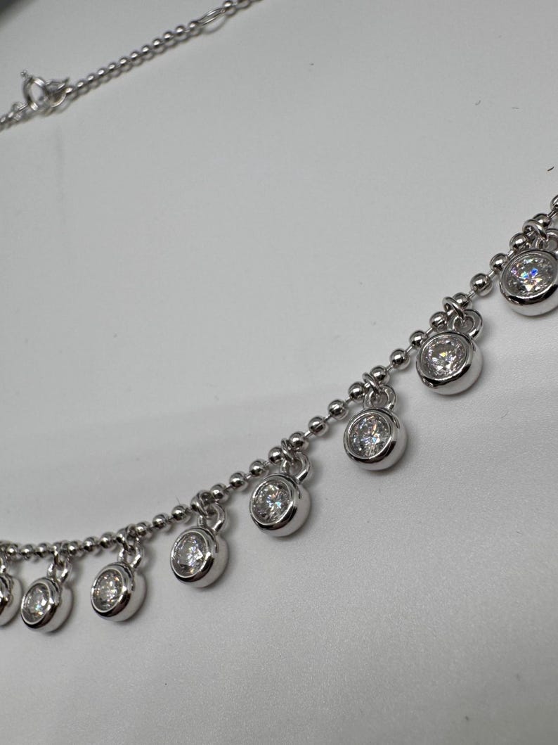 May include: A silver chain necklace with small round clear stones dangling from it.