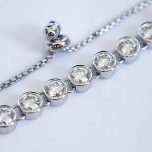 May include: A silver adjustable bracelet with a chain and round clear stones.