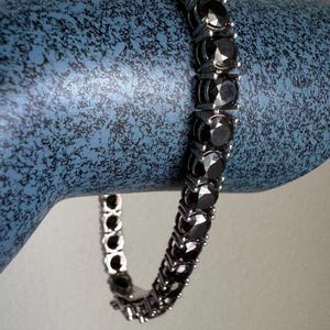 May include: A silver chain bracelet with black round gemstones. The bracelet is on a blue display stand.
