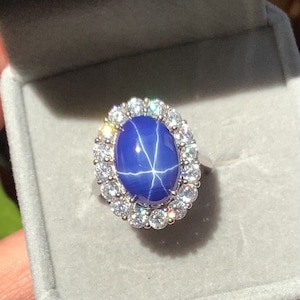 May include: A silver ring with a large blue star sapphire surrounded by a halo of smaller diamonds.