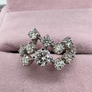 May include: A silver ring with a cluster of round, clear diamonds set in a wave-like pattern.