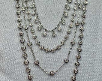 May include: A silver necklace with multiple strands of small round stones. The necklace has a layered look with a cascading effect.