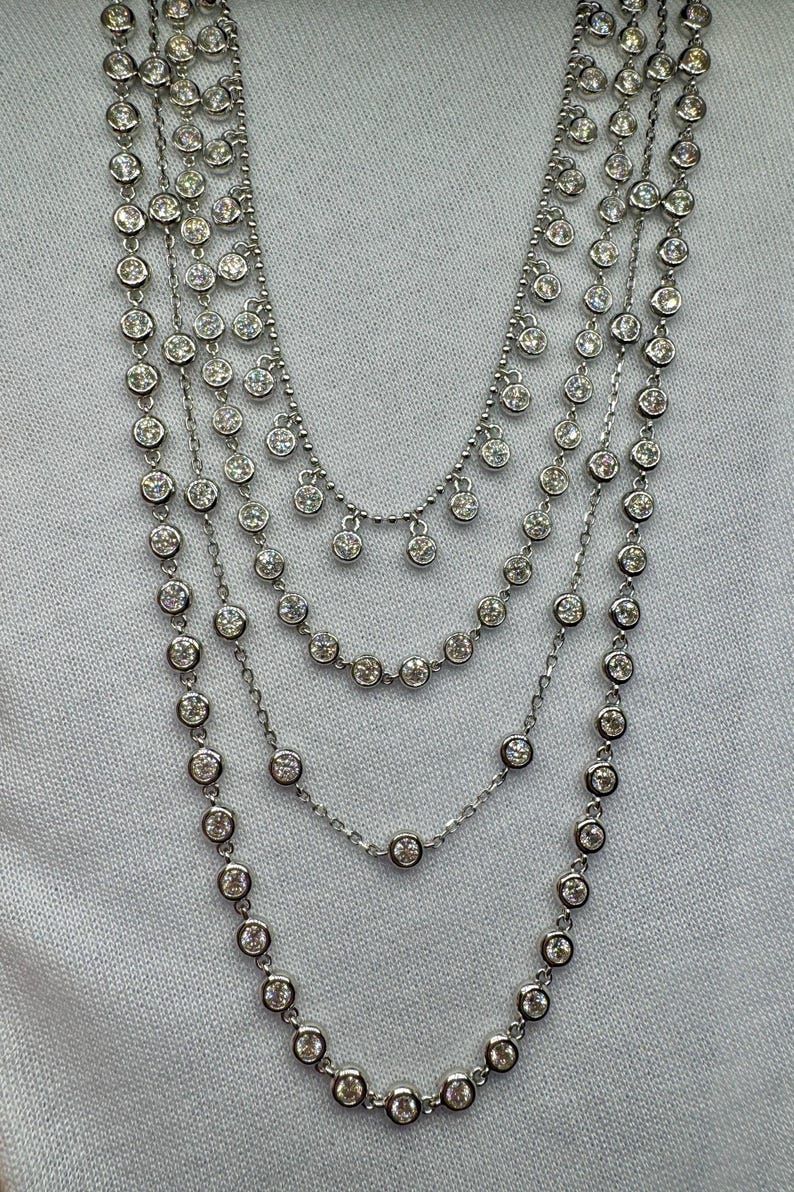 May include: A silver necklace with multiple strands of small round stones. The necklace has a layered look with a cascading effect.