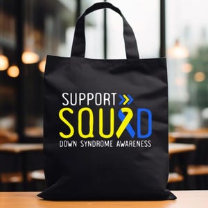 May include: Black tote bag with white text that reads "Support Squad" with a yellow and blue ribbon. The text "Down Syndrome Awareness" is below the ribbon.