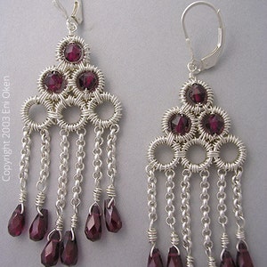 May include: Silver dangle earrings with a geometric design featuring multiple circles and dangling chains. The earrings are adorned with deep red gemstone beads.
