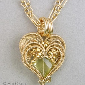 Może przedstawiać: Naszyjnik z zawieszką w kształcie serca owiniętym złotym drutem, z jasnozielonym kamieniem szlachetnym w środku. Zawieszka wykonana jest z delikatnej pracy z drutu i ma szczegółowy wzór.
