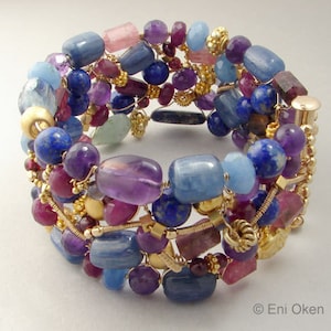 May include: A multi-strand bracelet featuring a variety of gemstones, including amethyst, lapis lazuli, aquamarine, and kyanite. The bracelet is wrapped in gold wire and features gold beads.