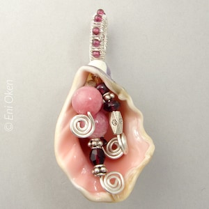 May include: A pink seashell pendant with a silver wire wrapped around the top. The shell is filled with pink and purple beads, silver wire spirals, and a silver charm.