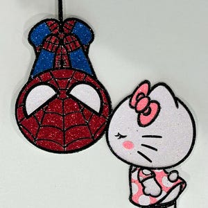 May include: A red and blue glitter Spiderman character hanging upside down with a white glitter Hello Kitty character with pink accents and a pink bow.