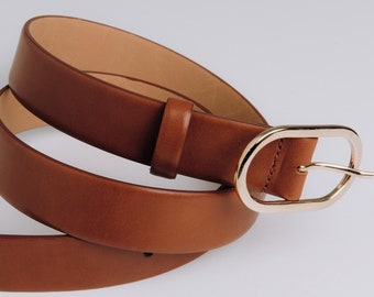 Peut inclure: Une ceinture en cuir marron avec une boucle ovale dorée. La ceinture est enroulée et prête à être portée.