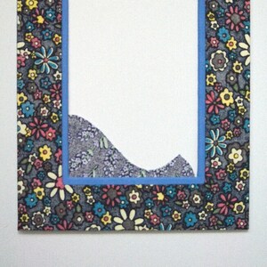 May include: A blue frame with a floral pattern surrounds a white background. The frame is made of fabric with a floral print in shades of pink, yellow, blue, and white. The floral pattern is repeated throughout the frame.