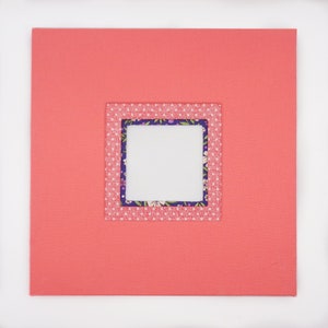 May include: A coral pink scrapbook with a square window cut out. The window is decorated with a white fabric with pink polka dots and a floral pattern.