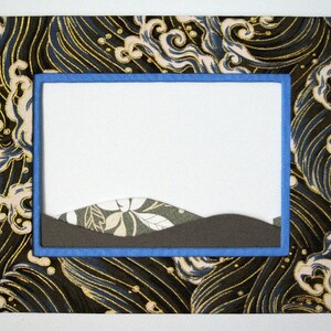 May include: A blue frame with a wave pattern border surrounds a blank space. The frame is made of fabric with a gold and black design. The blank space is filled with a brown and white landscape.