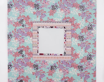 May include: A light blue fabric picture frame with a floral pattern and a white inner frame. The frame has a decorative border with pink, purple, and white accents.