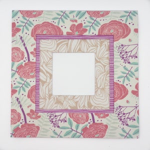 May include: A square picture frame with a floral pattern in shades of pink, green, and white. The frame has a double border, one in a light pink and the other in a darker pink.