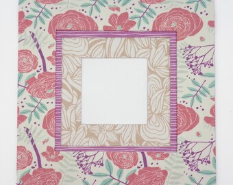 May include: A square picture frame with a floral pattern in shades of pink, green, and white. The frame has a double border, one in a light pink and the other in a darker pink.