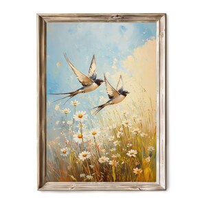 Könnte beinhalten: Gerahmtes Gemälde, das zwei Schwalben im Flug über einem Feld weißer Gänseblümchen zeigt. Das Kunstwerk zeigt einen hellblauen Himmel mit gelben und weißen Highlights, und der Rahmen hat ein rustikales, verwittertes Aussehen.