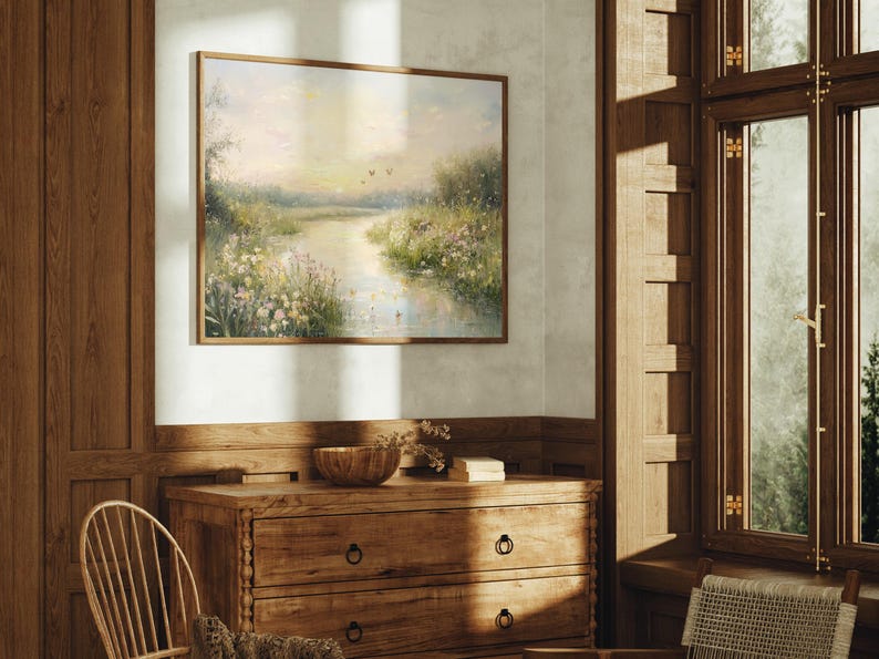 May include: A framed painting of a landscape with a river winding through a field of wildflowers. The painting is in a light brown frame and hangs on a white wall.