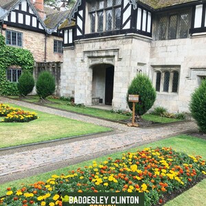 May include: Exterior view of a historic building with a stone facade and black and white timber framing. A brick pathway leads through a garden with vibrant yellow and orange flowers. The text "BADDESLEY CLINTON FRENCH" is displayed.