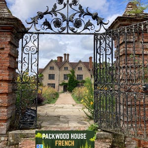 May include: An open, ornate black wrought iron gate leads to a stone path and a large, light-colored building. The gate is flanked by brick pillars. A sign at the base of the gate reads "PACKWOOD HOUSE FRENCH". The sky is blue with clouds.