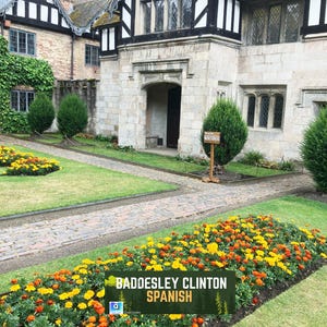 May include: Exterior view of a historic building with a stone facade and a black and white timbered gable. A flower bed with orange and yellow flowers lines a brick pathway. The text "Baddesley Clinton Spanish" is displayed on a green banner.