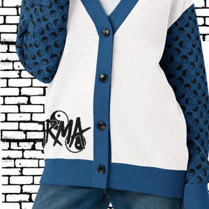 Könnte beinhalten: Weiß-blaue Strickjacke mit schwarzen Knöpfen. Die Ärmel haben ein Muster aus schwarzen und weißen Yin-Yang-Symbolen. Auf der Vorderseite des Pullovers steht das Wort "RMA" in schwarzer Schrift.