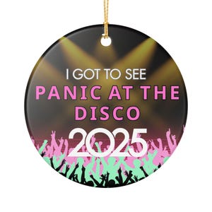 May include: Round ceramic ornament with a gold string for hanging. The ornament features the text "I GOT TO SEE PANIC AT THE DISCO 2025" in white and pink, with a crowd silhouette in the foreground.