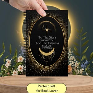 May include: Black spiral notebook with gold accents and the text "To The Stars Who Listen And The Dreams That Are Answered." The notebook has a gold oval design with stars and a crescent moon. The words "Perfect Gift for Book Lover" are on a yellow label.