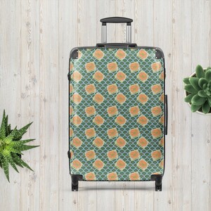 May include: A patterned suitcase featuring a repeating design of orange squares on a teal and blue background. The suitcase has a retractable handle and black wheels. The design evokes a vintage travel style.