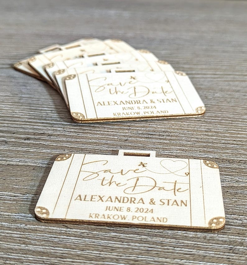 Puede incluir: Peque&ntilde;os recuerdos de boda de madera en forma de maleta, grabados con "Save the Date", nombres, fecha y lugar. La fecha es el 8 de junio de 2024. Se ven detalles decorativos en las esquinas.