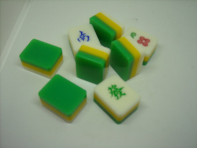 May include: A set of six green, yellow, and white mahjong tiles. The tiles have Chinese characters and a flower design.