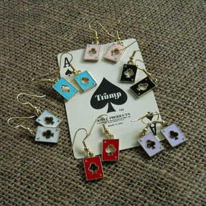 May include: A set of eight pairs of gold-tone earrings featuring playing card designs. The earrings feature a variety of suits, including hearts, clubs, spades, and diamonds. The cards are in various colors, including red, black, blue, and white.