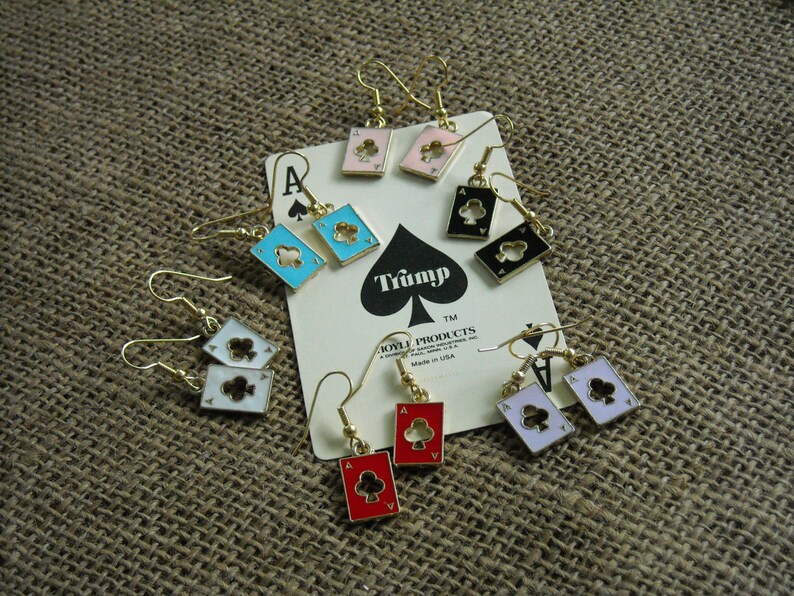 May include: A set of eight pairs of gold-tone earrings featuring playing card designs. The earrings feature a variety of suits, including hearts, clubs, spades, and diamonds. The cards are in various colors, including red, black, blue, and white.