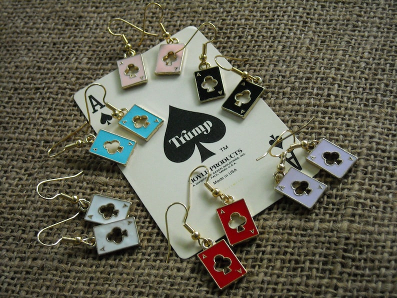 May include: A set of eight pairs of gold-tone earrings featuring playing card designs. Each earring features a different card suit: hearts, diamonds, clubs, and spades. The cards are in various colors, including red, black, blue, white, and pink.