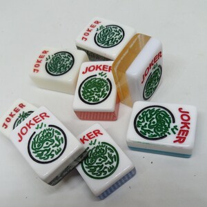 May include: A collection of white Mahjong tiles with green and black circular designs. Each tile has the word "JOKER" in red. Some tiles have colored edges, including pink, blue, and orange.