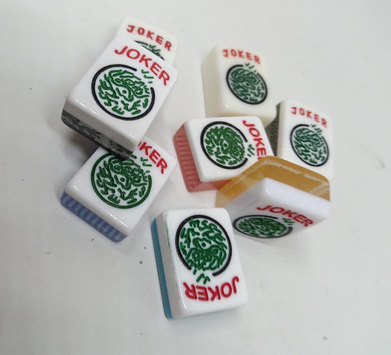 May include: A collection of white Mahjong tiles with the word "JOKER" in red. Each tile features a green circular design. Some tiles have colored edges in blue, pink, and orange.