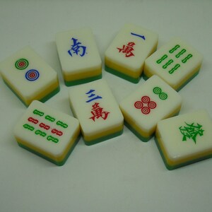 May include: A set of nine Chinese dominoes, also known as mahjong tiles. The tiles are white with green, red, and blue markings. Some tiles have Chinese characters, while others have dots or lines.