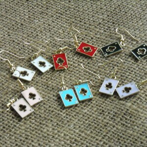 May include: A set of 10 pairs of earrings featuring a playing card design. The earrings are made of gold-tone metal and feature a variety of colors, including red, black, white, blue, and pink. Each earring features a different playing card suit, including clubs, diamonds, hearts, and spades.