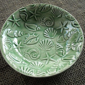 May include: A green ceramic bowl with a raised design of seashells and starfish. The bowl is glazed and has a glossy finish.