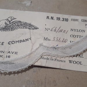 May include: A white lace trim with a label that reads "ESKELL LACE COMPANY 79. MADISON AVE NEW-YORK 16 R.N. 19.310 FIBRE CONTENTS PER CENT N°64/1001 NYLON COTTO Mts 33120 ST FAL Made in France WOOL."