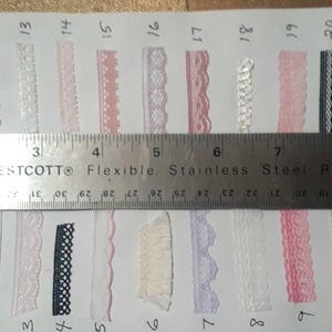 May include: A variety of decorative lace trims in various colors and designs are displayed on a white surface. A metal ruler shows measurements in inches. The lace trims include floral, scalloped, and geometric patterns, with a total of 42 yards.