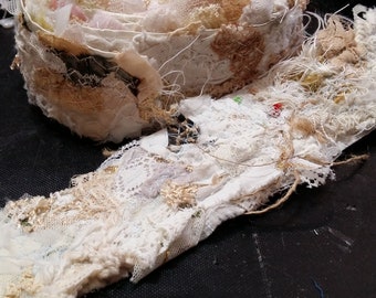May include: A close-up of a white and beige fabric trim with a delicate lace pattern. The trim is frayed and has a rustic, vintage look.
