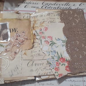 May include: A vintage-style journal with aged paper pages, featuring a small framed image and floral patterns. The journal includes a decorative lace edge and a cream-colored ribbon. The background includes ledger paper and handwritten text.