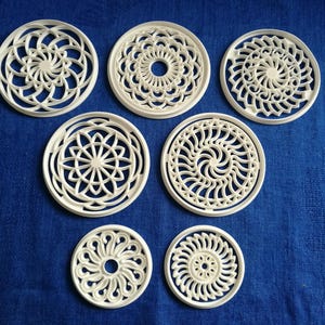 May include: Set of seven white plastic cookie cutters with intricate geometric designs. The cutters are round and feature different patterns, including swirls, circles, and stars.