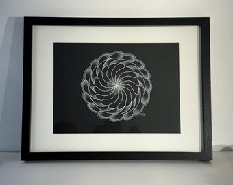 Op de afbeelding: Een zwart-wit ingelijste print van een wit geometrisch ontwerp op een zwarte achtergrond. Het ontwerp is een spiraal van witte vormen die lijken op bloemblaadjes.