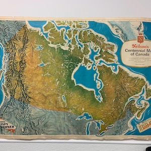 May include: Vintage map of Canada, titled "Nielson's Centennial Map of Canada." The map features a detailed depiction of the country's geography, with shades of blue, green, and brown. The map includes the text "Nielson's Crispy Crunch" and "Jersey Butter."