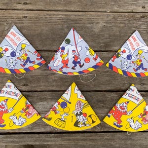 May include: Six colourful paper party hats with a circus theme. The hats are decorated with clowns, animals, and the text "Bonne Fete Happy Birthday".